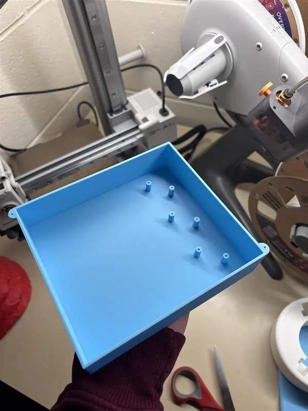 Freshly 3D-printed blue macro pad enclosure held in front of a 3D printer